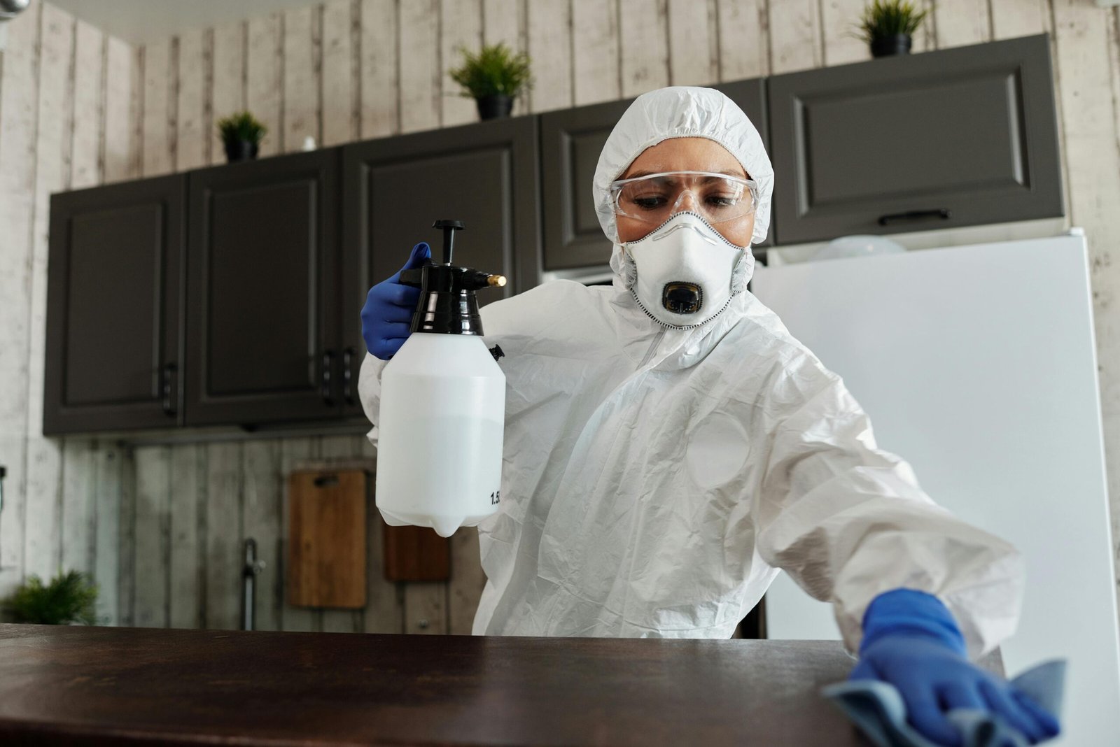 A woman in protective gear disinfecting an indoor area using a spray bottle.